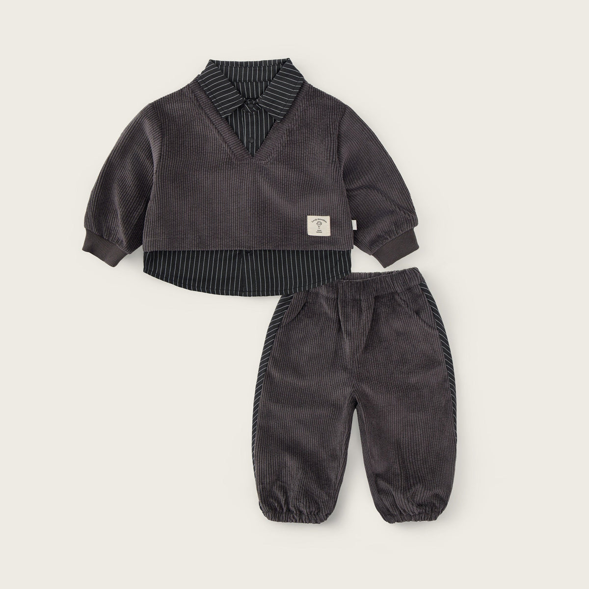A baby clothing set from Jacinda Bebe, featuring a dark gray corduroy long-sleeve top with a striped shirt collar and matching corduroy pants, displayed on a light beige background with brand text.