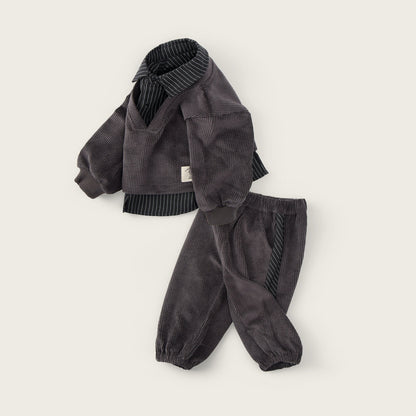 A children's two-piece corduroy outfit in dark gray, featuring a cropped jacket with ribbed knit collar and hem, and matching jogger pants, displayed on a light beige background with 'jacinda bebe' and 'lovely kids' text.