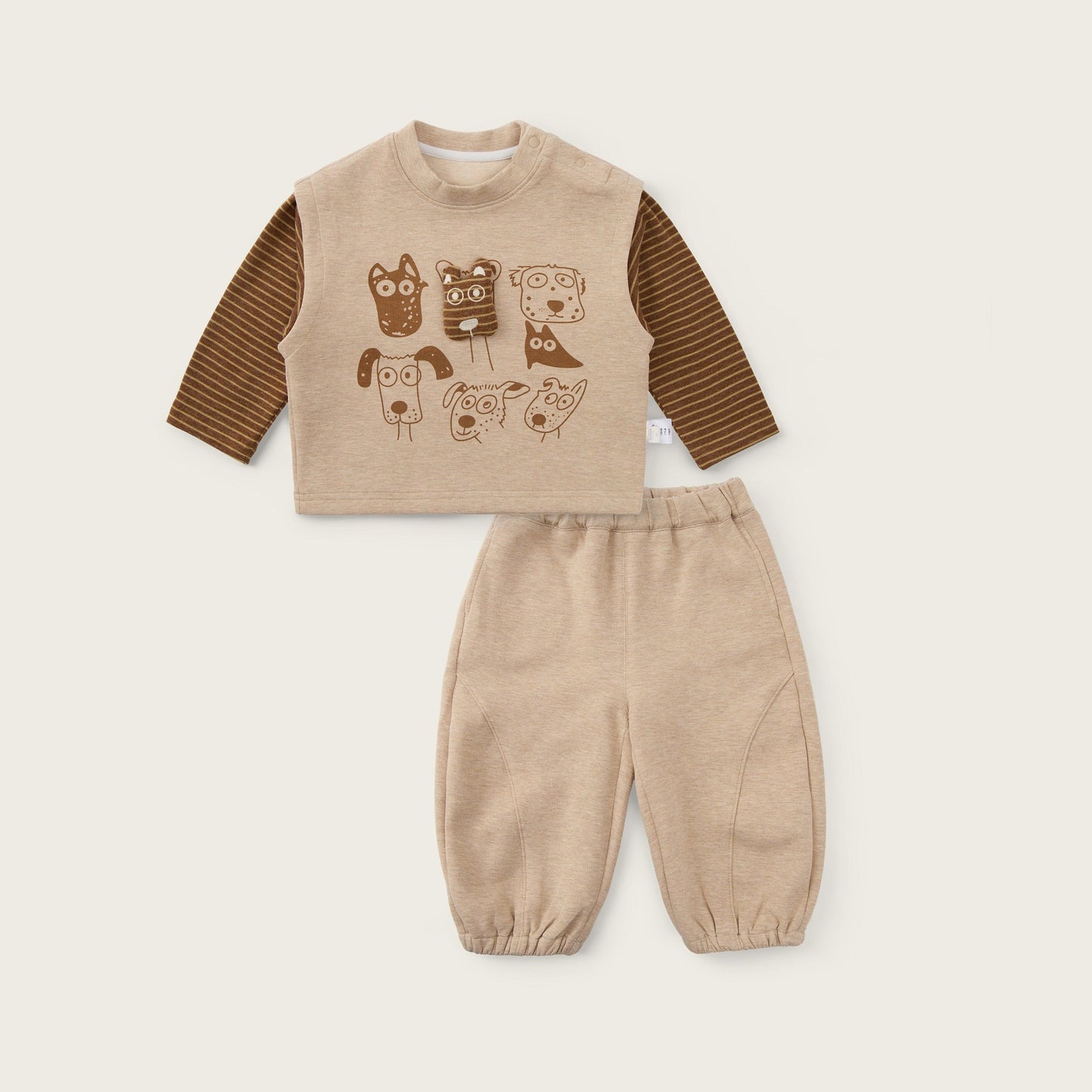 A toddler two-piece outfit set featuring a beige long-sleeve top with brown striped sleeves and a dog-themed graphic print, paired with matching beige pants, displayed on a light beige background with 'jacinda bebe' and 'lovely kids' text.