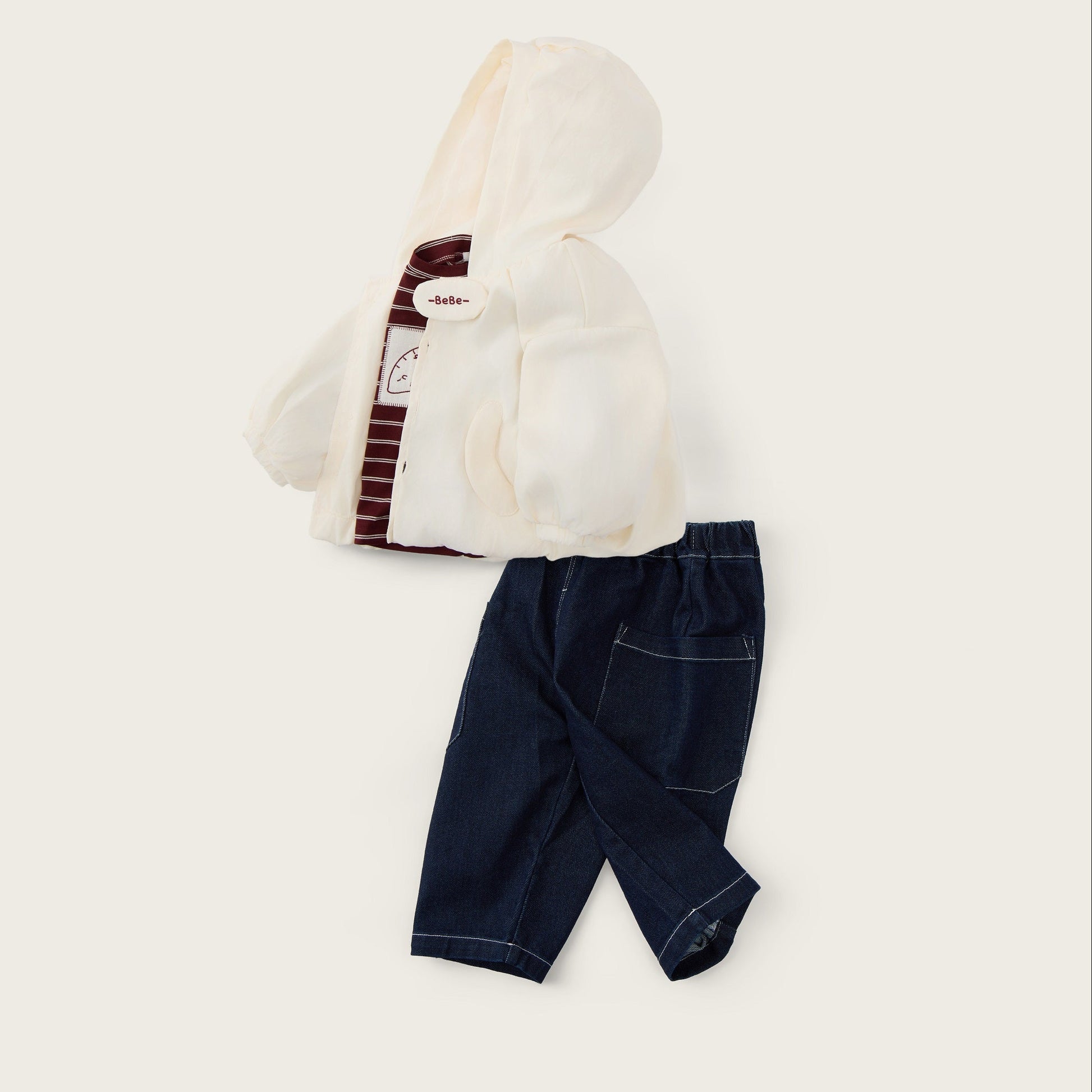 A baby clothing set featuring an off-white hooded cardigan with a striped collar detail and dark navy blue pants, laid flat on a light beige background with 'jacinda bebe' and 'lovely kids' text.