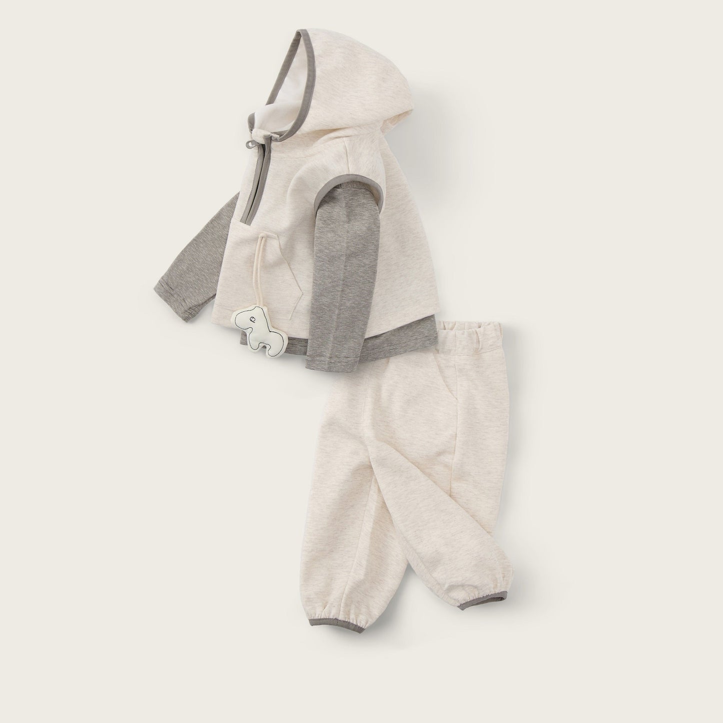 A baby clothing set laid flat on a warm off-white background, featuring a cream hooded vest with gray sleeves and matching cream pants. The text 'jacinda bebe' appears at the top and 'lovely kids' at the bottom.