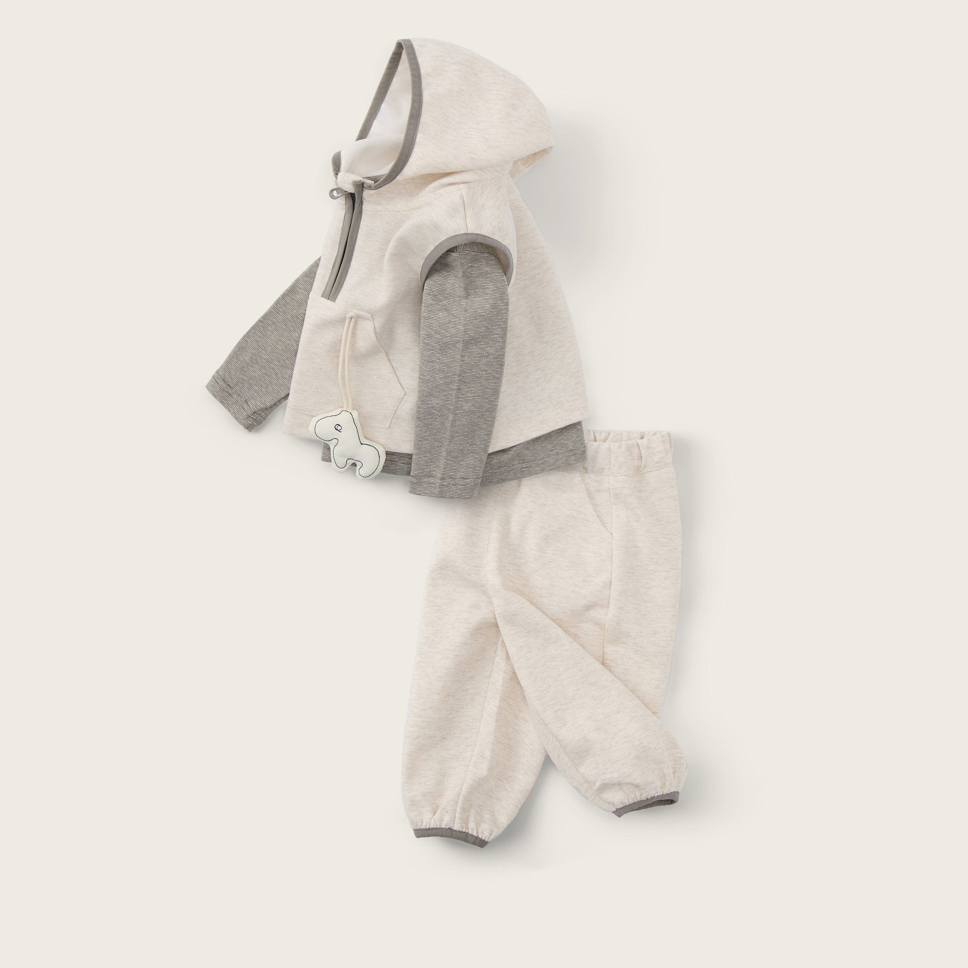 A baby clothing set laid flat on a warm off-white background, featuring a cream hooded vest with gray sleeves and matching cream pants. The text 'jacinda bebe' appears at the top and 'lovely kids' at the bottom.