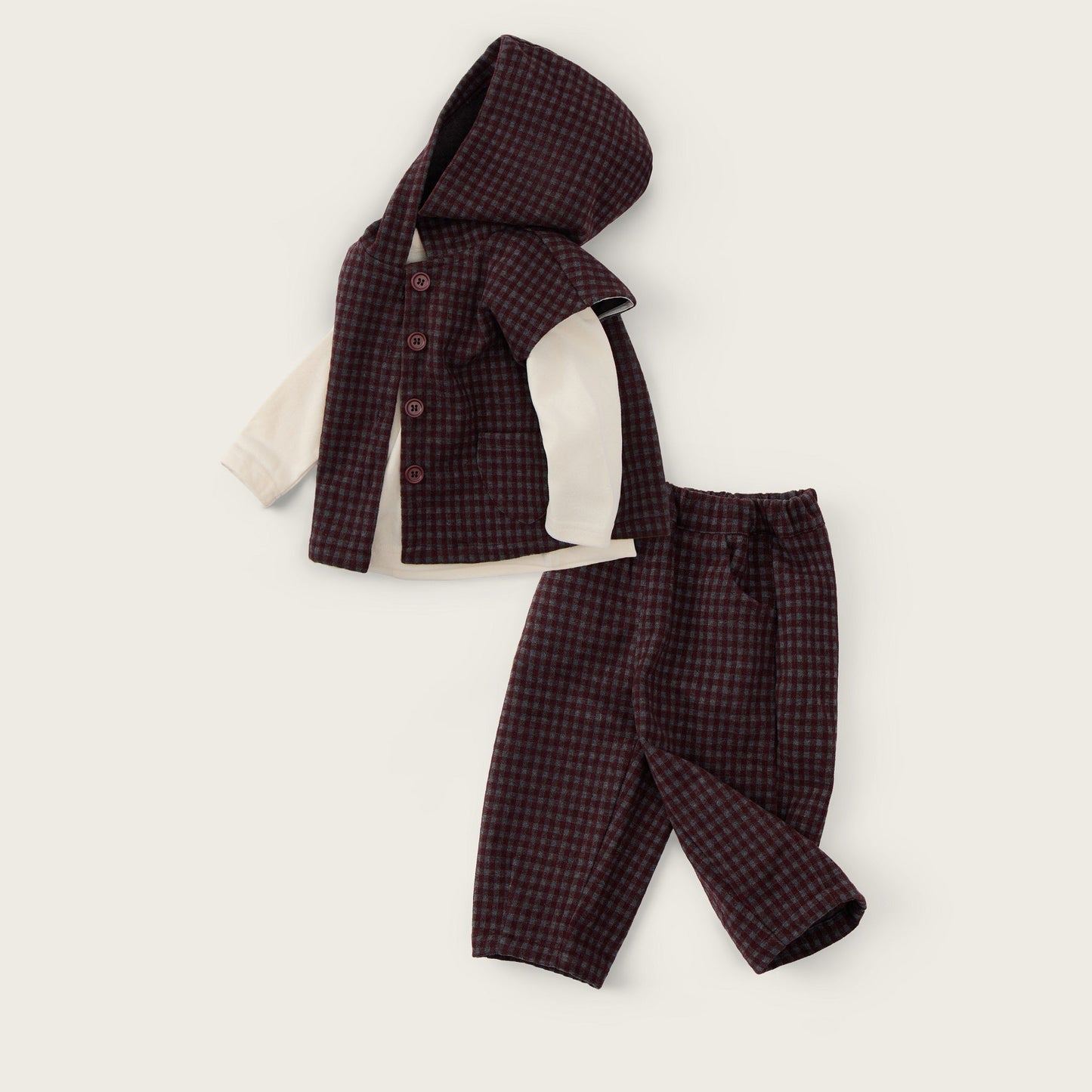 A baby clothing set laid flat on a light cream background, featuring a dark burgundy and black checkered hooded vest over a cream long-sleeve shirt, paired with matching checkered pants. The text 'jacinda bebe' appears at the top and 'lovely kids' at the bottom.