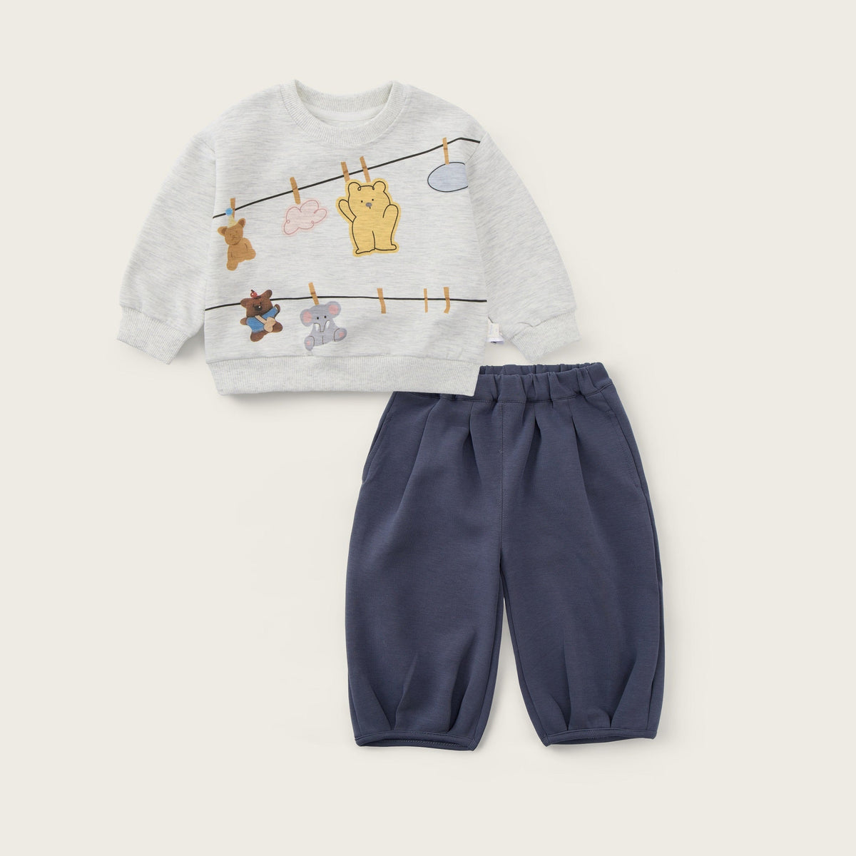A children's two-piece outfit set featuring a light gray long-sleeve sweatshirt with a cartoon laundry-line and animal print, paired with navy blue jogger pants. The brand text 'jacinda bebe' is displayed at the top and 'lovely kids' at the bottom on a light beige background.