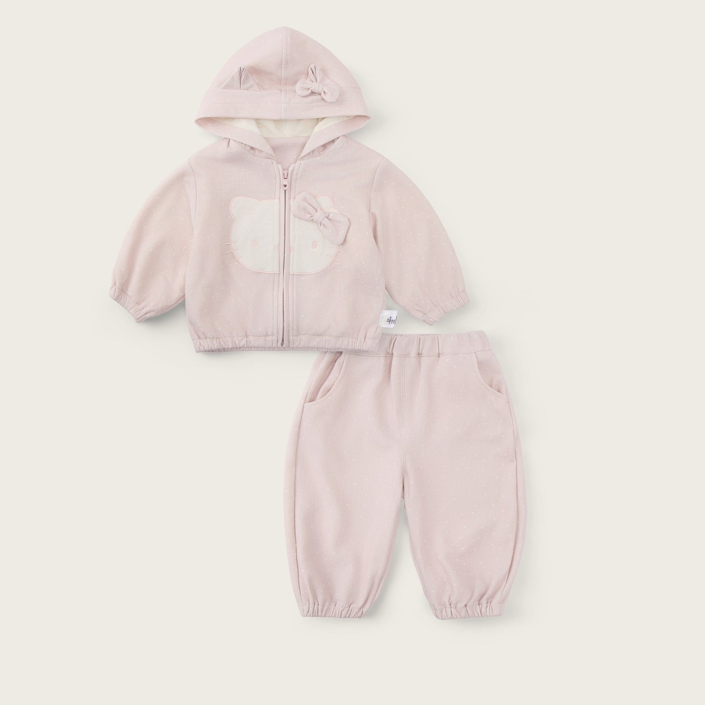A baby girl's two-piece clothing set in a soft light pink, featuring a zip-up hooded jacket with a bear face applique and matching jogger pants. The set is displayed flat on a warm off-white background with 'jacinda bebe' written at the top and 'lovely kids' at the bottom.