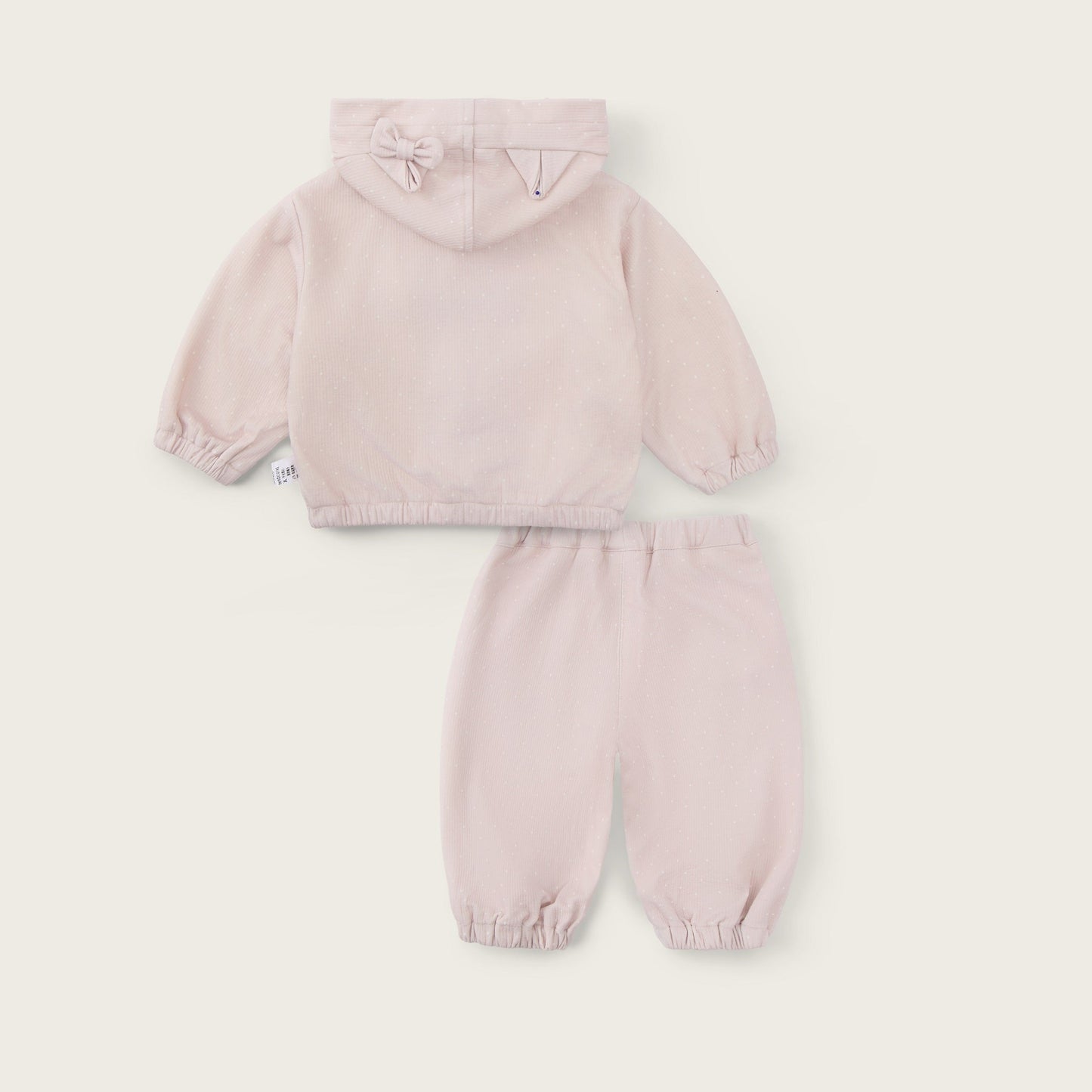A two-piece baby outfit set in a very pale blush pink, featuring a hooded sweatshirt and matching jogger pants, displayed on a light cream background with 'jacinda bebe' and 'lovely kids' text.