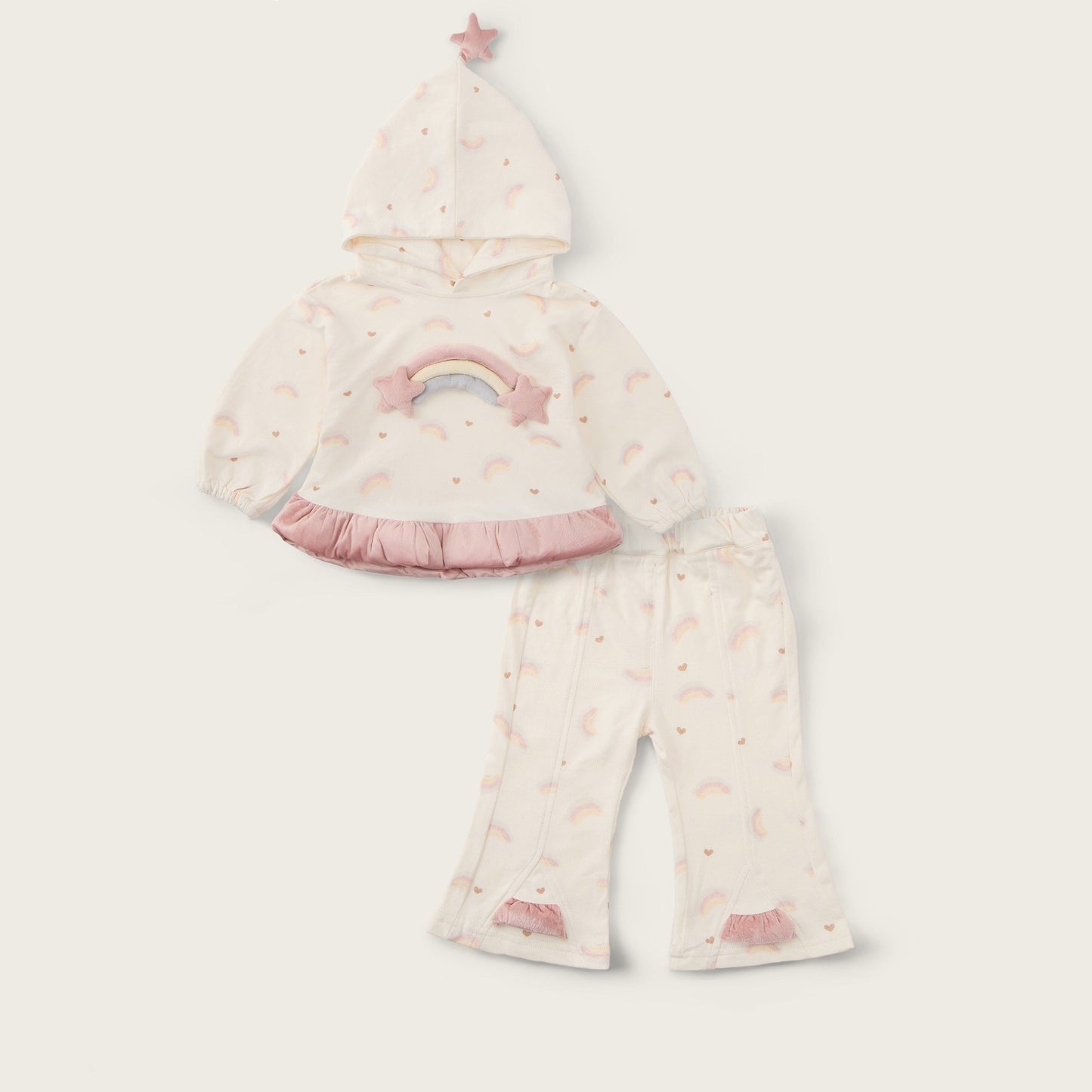 A baby girl's two-piece pajama set from Jacinda Bebe, featuring a hooded top with a pastel rainbow and star print, and matching flared pants, displayed on a light beige background with brand text.