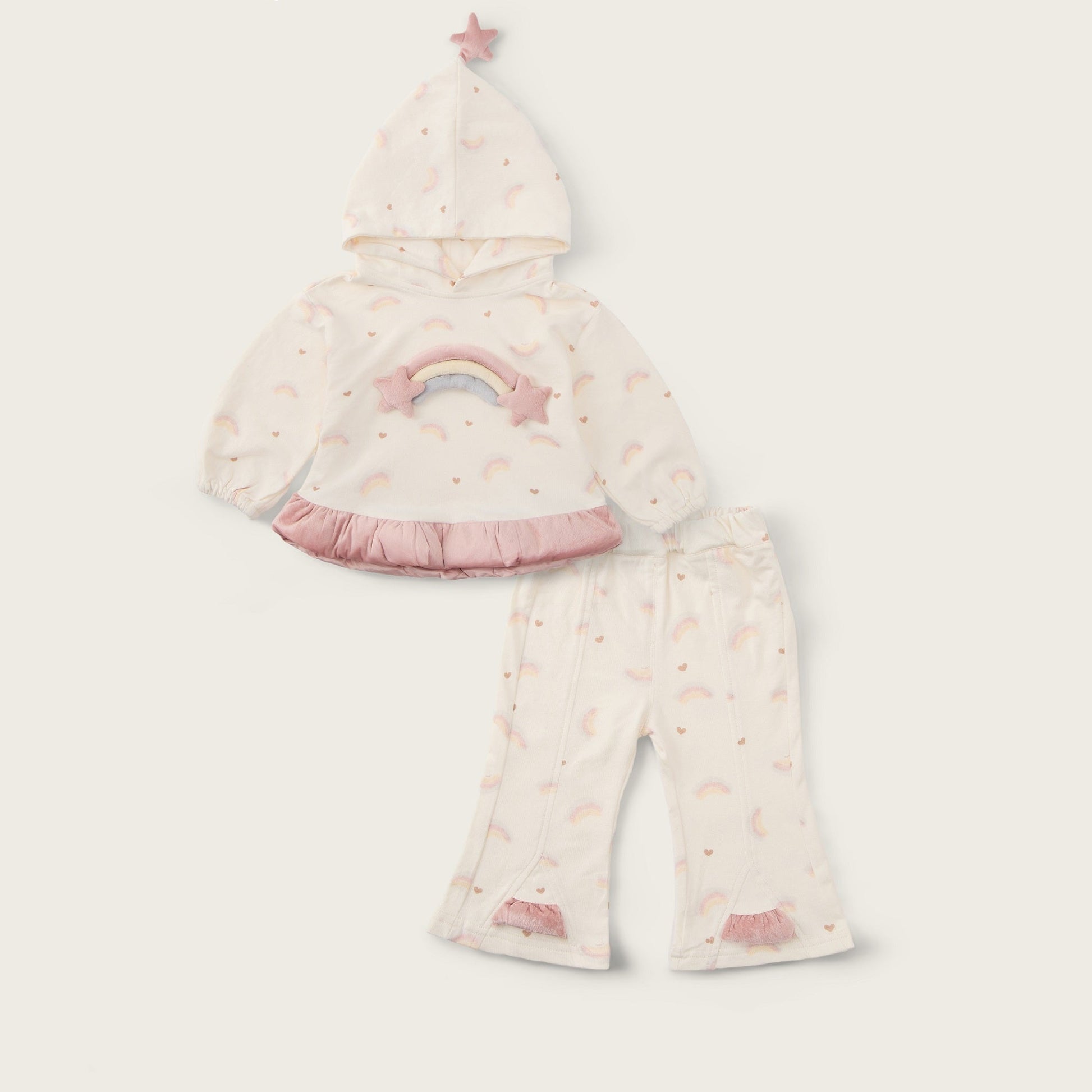 A baby girl's two-piece pajama set from Jacinda Bebe, featuring a hooded top with a pastel rainbow and star print, and matching flared pants, displayed on a light beige background with brand text.