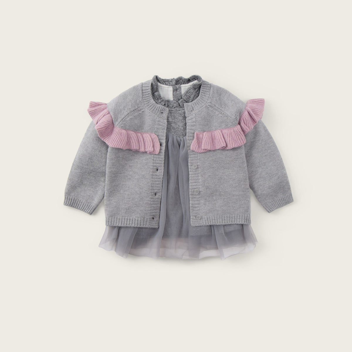 A baby girl's gray knit cardigan with pink ruffle accents on the shoulders, layered over a matching gray tulle dress, shown against a light beige background with 'jacinda bebe' and 'lovely kids' text.