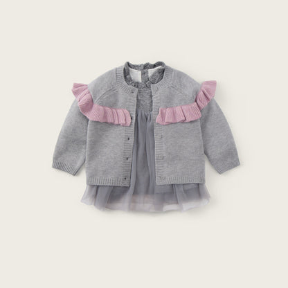 A baby girl's gray knit cardigan with pink ruffle accents on the shoulders, layered over a matching gray tulle dress, shown against a light beige background with 'jacinda bebe' and 'lovely kids' text.