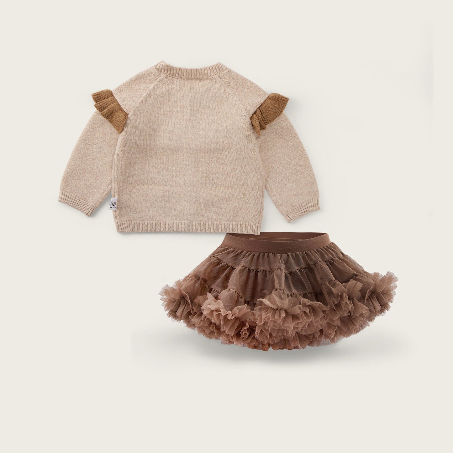 A baby clothing set featuring a beige knit sweater with brown ruffle details on the shoulders and a matching brown ruffled tutu skirt, displayed on a light beige background with 'jacinda bebe' at the top and 'lovely kids' at the bottom.