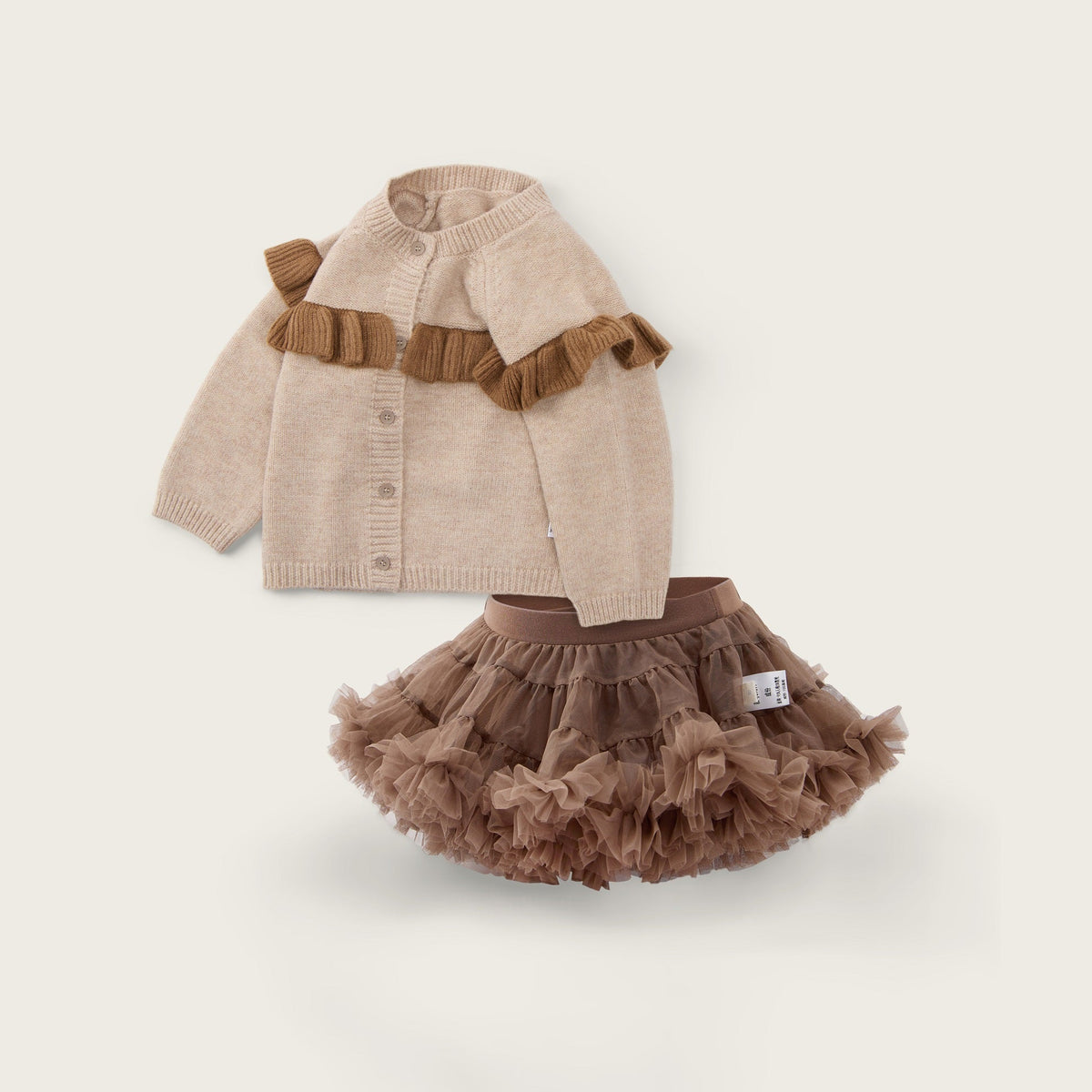 A baby girl's two-piece outfit set featuring a beige knit cardigan with brown ruffle accents and a matching brown ruffled tutu skirt, displayed on a light beige background with 'jacinda bebe' and 'lovely kids' text.