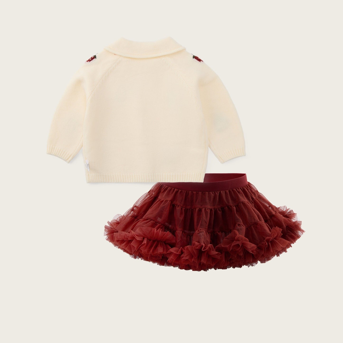 A baby girl's two-piece outfit set featuring a cream knit mock-neck sweater with small red shoulder details and a matching dark red ruffled tutu skirt, displayed on a light beige background with 'jacinda bebe' and 'lovely kids' text.