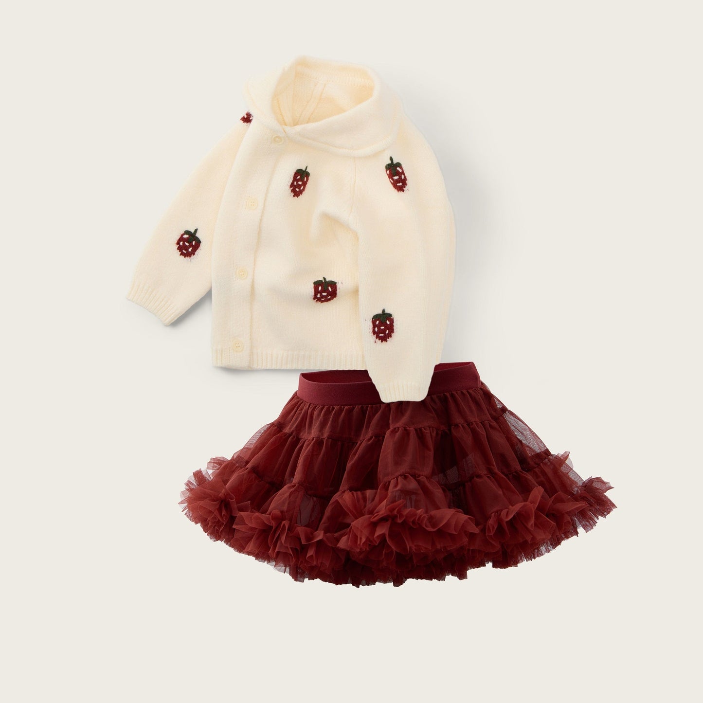 A baby girl's two-piece outfit set featuring a cream knit cardigan with embroidered red strawberries and a matching dark red ruffled tutu skirt, displayed on a light beige background with 'jacinda bebe' and 'lovely kids' text.