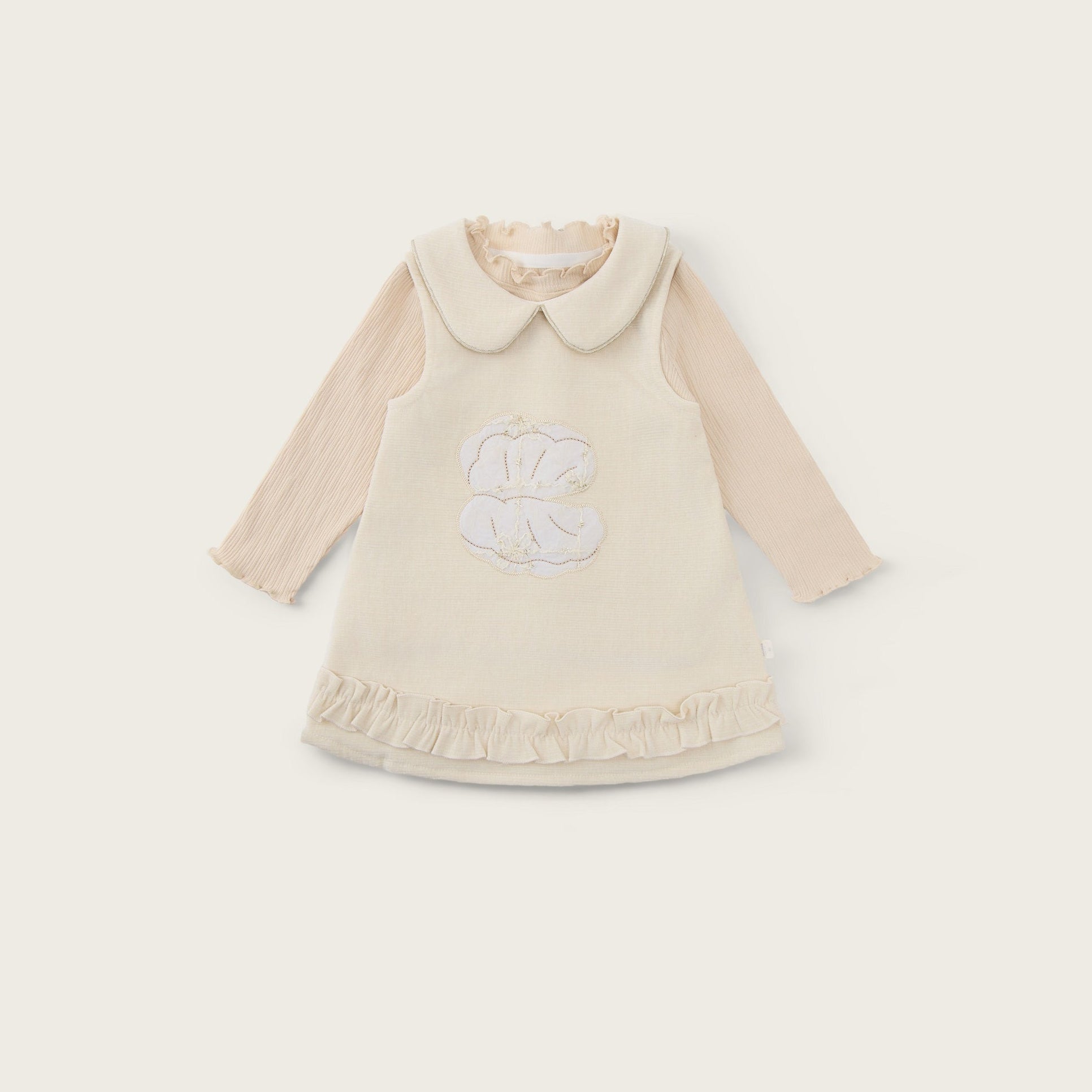 A cream-colored baby dress with long beige sleeves, a Peter Pan collar, and a white embroidered monogram on the front, displayed on a light beige background with 'jacinda bebe' at the top and 'lovely kids' at the bottom.