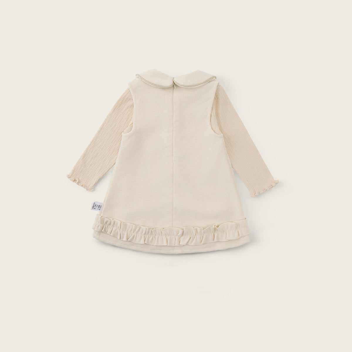A baby long-sleeve dress in cream and beige, featuring a ruffled hem and a Peter Pan collar, shown from the back on a light beige background with 'jacinda bebe' and 'lovely kids' text.