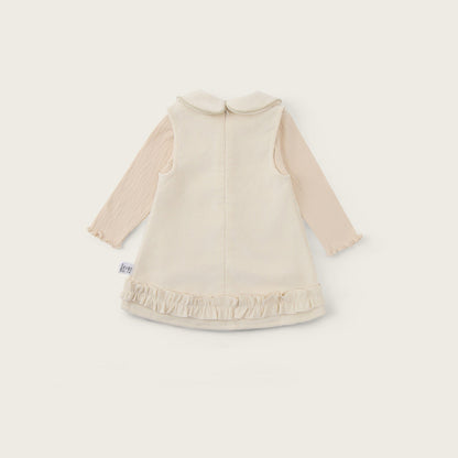 A baby long-sleeve dress in cream and beige, featuring a ruffled hem and a Peter Pan collar, shown from the back on a light beige background with 'jacinda bebe' and 'lovely kids' text.