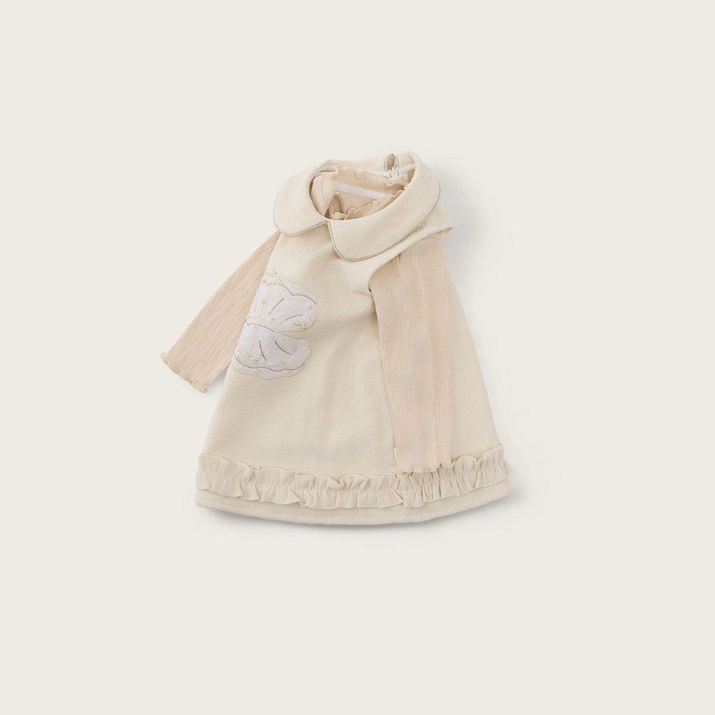 A cream-colored baby cape with a wide collar and a white embroidered flower on the chest, displayed on a light beige background with 'jacinda bebe' at the top and 'lovely kids' at the bottom.