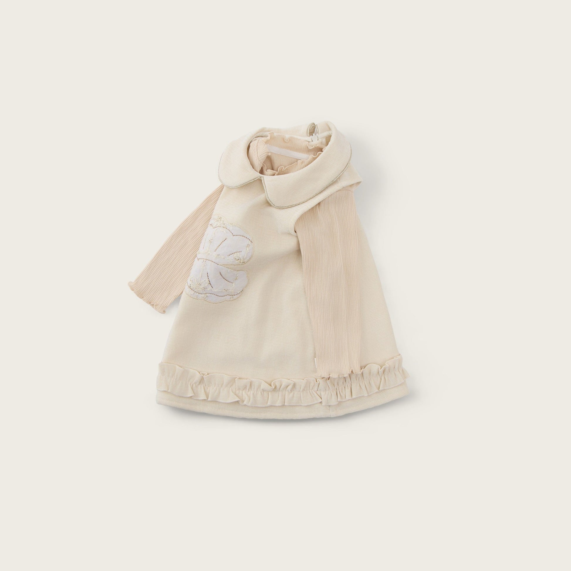 A cream-colored baby cape with a wide collar and a white embroidered flower on the chest, displayed on a light beige background with 'jacinda bebe' at the top and 'lovely kids' at the bottom.