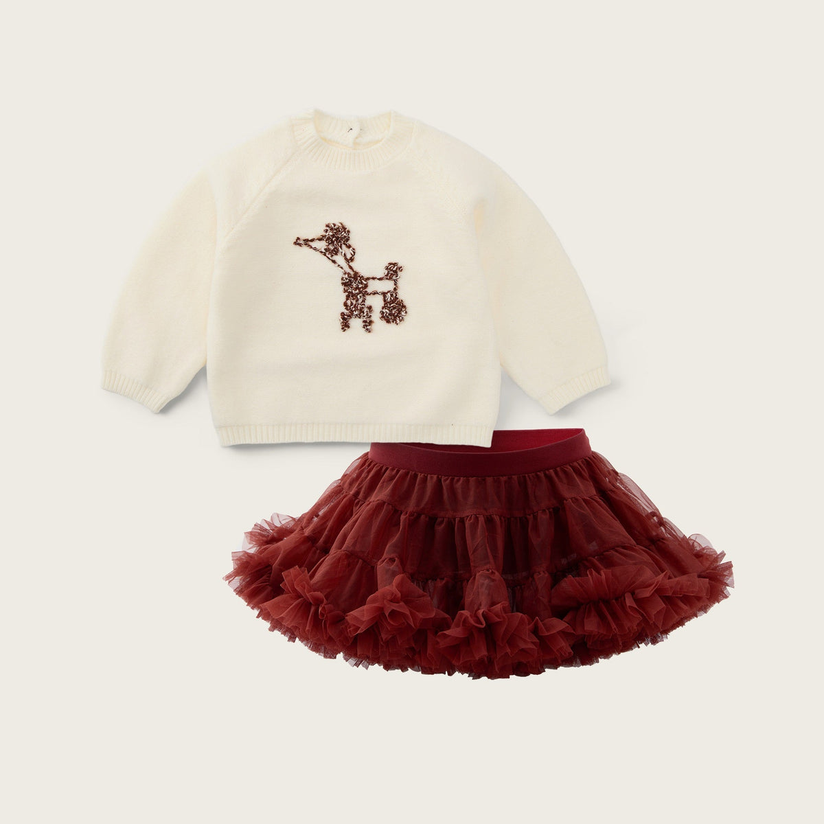 A baby girl's two-piece outfit set featuring an off-white long-sleeve knit top with a brown poodle patch and a matching dark red ruffled tutu skirt, displayed on a light beige background with brand text.