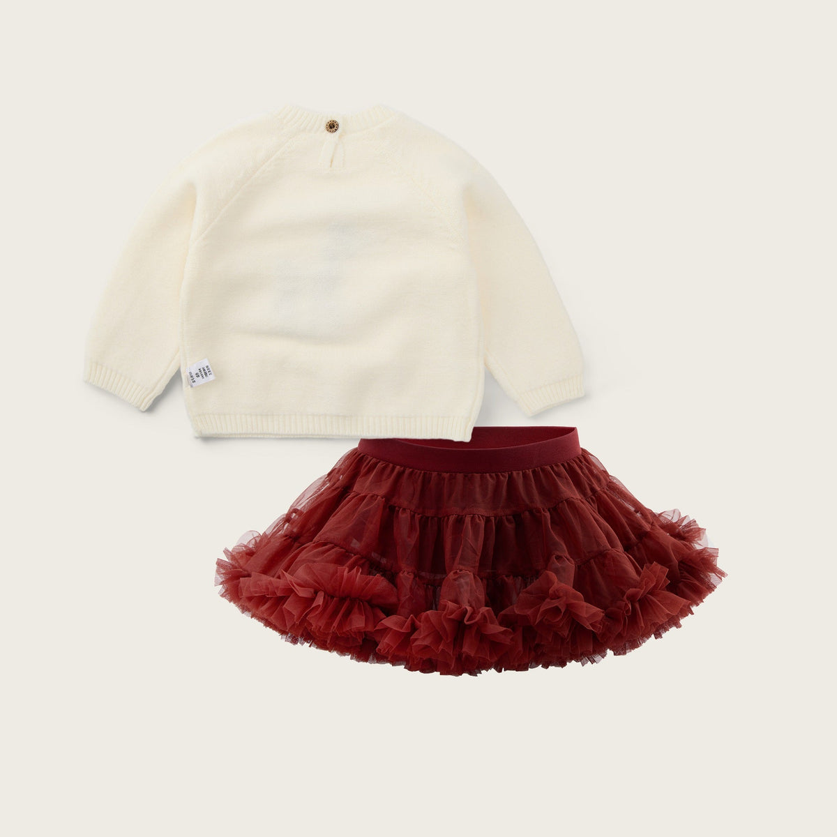A baby outfit set featuring an off-white long-sleeve knit top and a dark red ruffled tutu skirt, displayed on a light beige background with 'jacinda bebe' at the top and 'lovely kids' at the bottom.