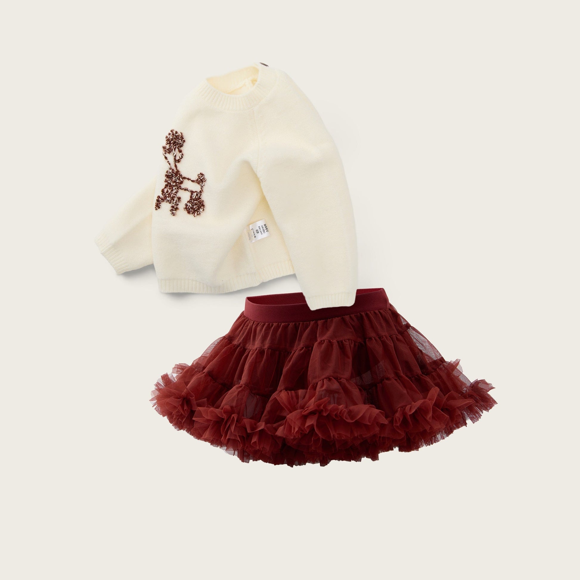 A children's outfit set featuring an off-white long-sleeve top with a brown embroidered dog design and a dark red ruffled tutu skirt, displayed on a light beige background with 'jacinda bebe' and 'lovely kids' text.