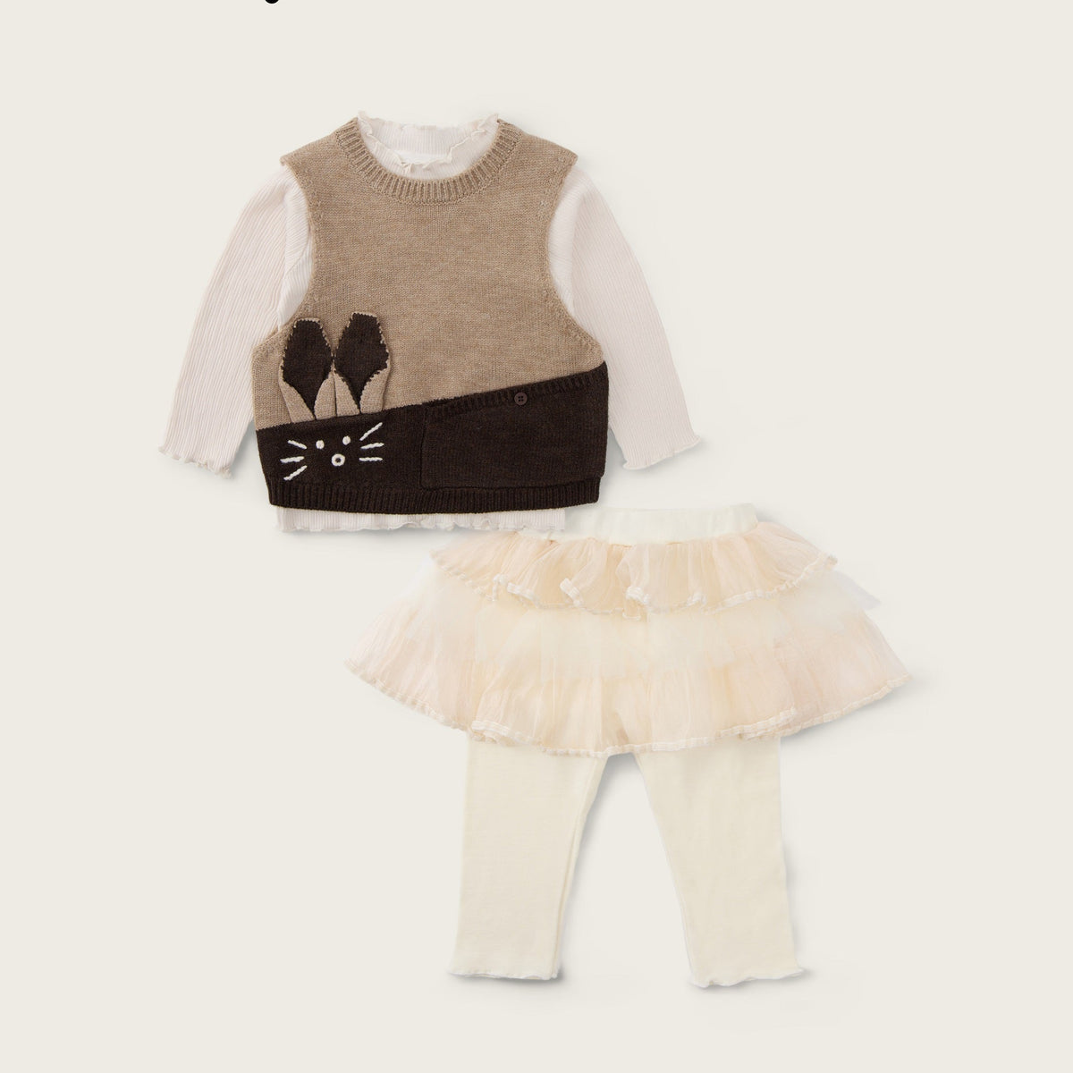 A baby girl's two-piece outfit set from Jacinda Bebe, featuring a knit vest with a cat face applique over a white long-sleeve shirt, paired with a ruffled cream tutu skirt and cream leggings. The brand logos 'jacinda bebe' and 'lovely kids' are displayed on the cream background.