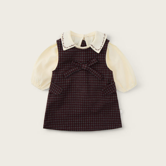 A baby girl's dress featuring a dark brown and red checkered pinafore vest over a cream-colored long-sleeve blouse with a lace-trimmed Peter Pan collar. The brand names 'jacinda bebe' at the top and 'lovely kids' at the bottom are printed on a light beige background.