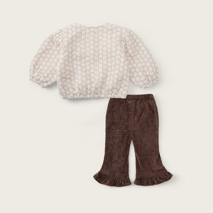 A two-piece baby outfit set featuring a cream-colored textured knit top with puff sleeves and dark brown corduroy flared pants with ruffle hems, displayed on a light beige background with 'jacinda bebe' and 'lovely kids' text.