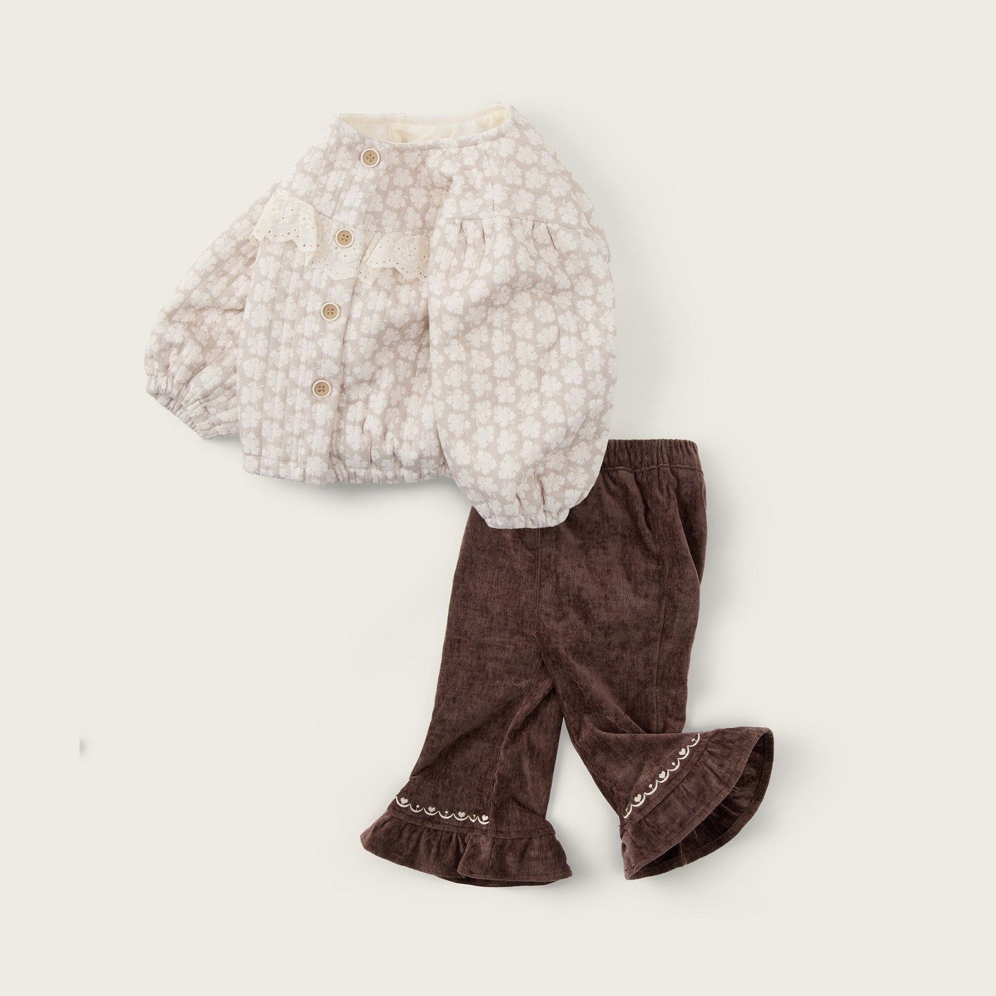 A baby outfit set featuring a cream-colored patterned long-sleeve cardigan and dark brown corduroy pants with ruffled cuffs, displayed on a light beige background with 'jacinda bebe' and 'lovely kids' text.