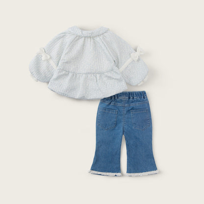 A toddler girl's two-piece outfit set featuring a white textured long-sleeve ruffle blouse with bow details and blue denim flare pants with white frayed hems, displayed on a light beige background with 'jacinda bebe' and 'lovely kids' text.