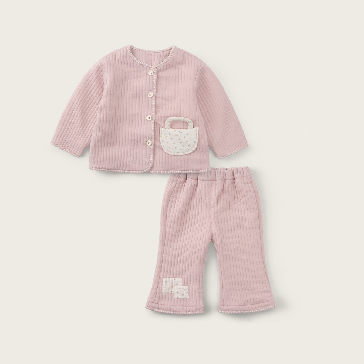 A baby girl's two-piece outfit set in light pink ribbed fabric, featuring a long-sleeve cardigan with a small white embroidered basket detail on the chest and matching ribbed pants, displayed on a warm off-white background with 'jacinda bebe' and 'lovely kids' text.