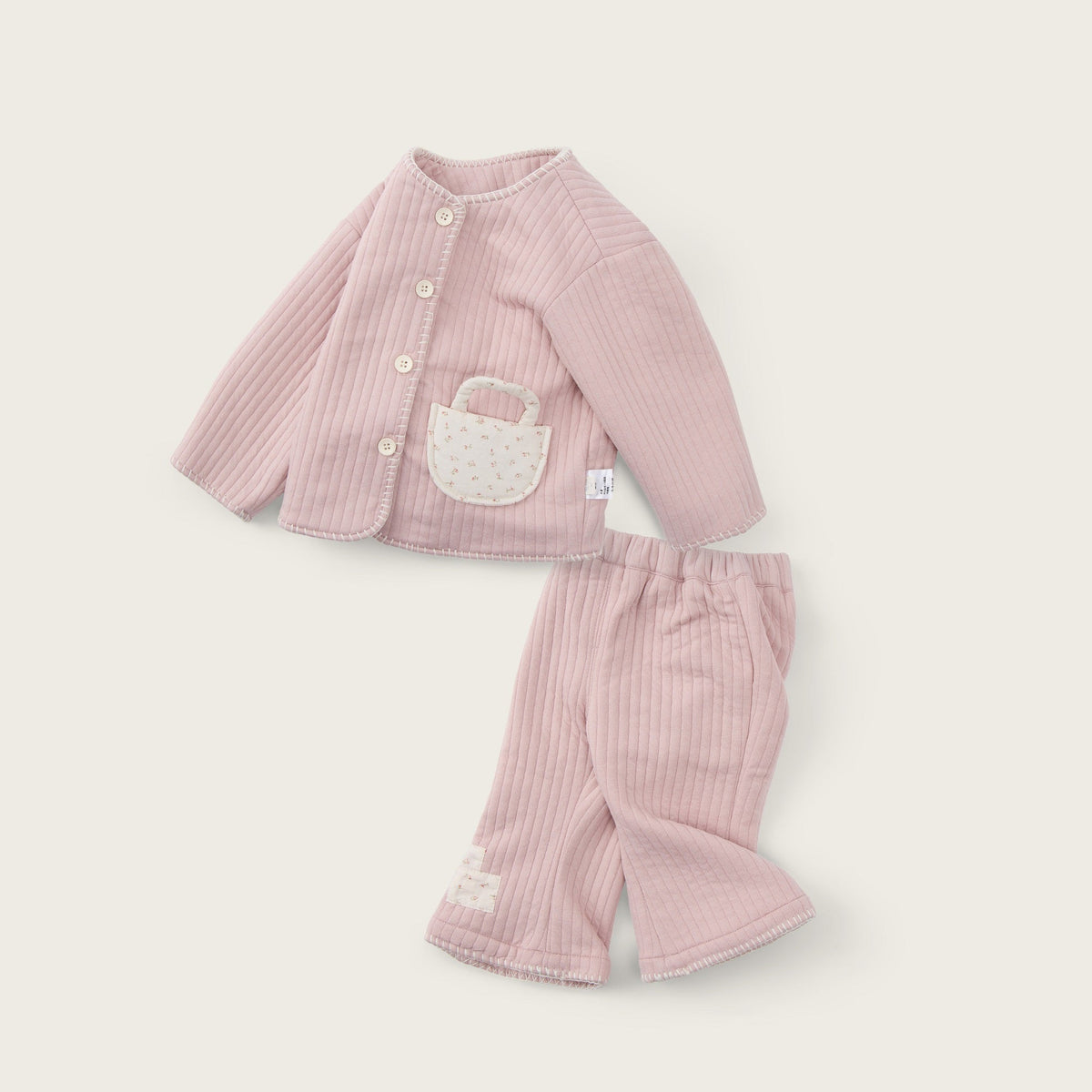 A two-piece baby outfit set in light pink ribbed corduroy, featuring a long-sleeve cardigan with a white embroidered basket detail on the chest and matching ribbed pants, displayed on a warm off-white background with 'jacinda bebe' and 'lovely kids' text.