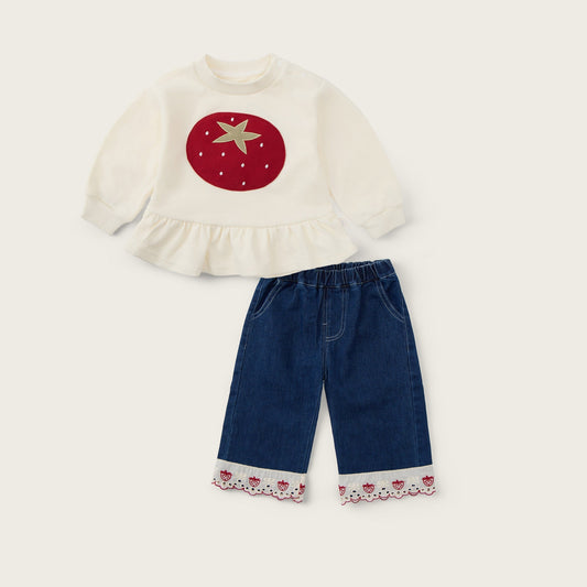 A children's two-piece outfit set featuring a cream long-sleeve top with a red strawberry and gold star applique, paired with dark blue denim pants that have a cream floral lace hem. The set is displayed on a light beige background with 'jacinda bebe' written at the top and 'lovely kids' at the bottom.