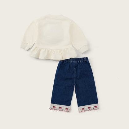 A two-piece baby outfit set featuring a cream long-sleeve ruffle-sleeve top and dark blue denim pants with a floral lace cuff, displayed on a light beige background with 'jacinda bebe' and 'lovely kids' text.