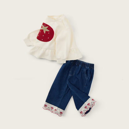 A baby girl's two-piece outfit set featuring a cream ruffled long-sleeve top with a red strawberry applique and dark blue denim-style pants with cream floral lace cuffs, displayed on a light beige background with 'jacinda bebe' and 'lovely kids' text.