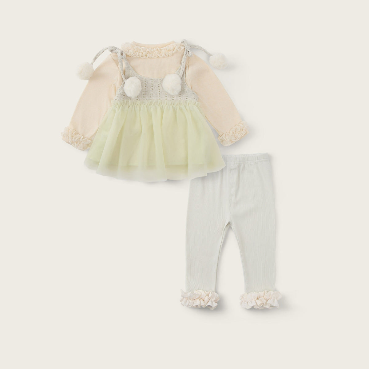 A baby girl's two-piece outfit set featuring a cream and pale yellow tulle dress with long sleeves and pom-pom details, paired with light gray leggings with ruffle cuffs. The image is presented on a warm cream background with 'jacinda bebe' at the top and 'lovely kids' at the bottom.
