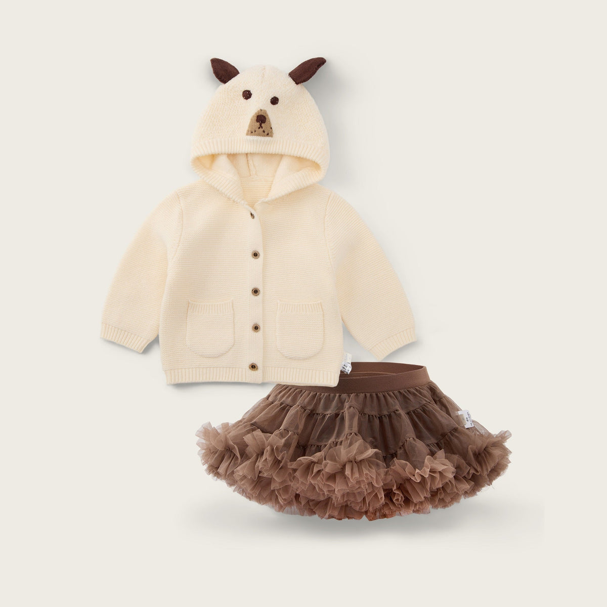 A children's outfit set featuring a cream-colored hooded cardigan with a bear face on the hood and brown ears, paired with a brown ruffled tutu skirt, shown on a light beige background with the text 'jacinda bebe' and 'lovely kids'.