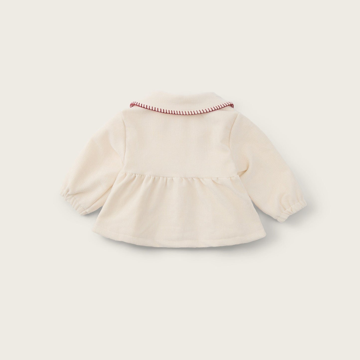 A cream-colored long-sleeve baby top with a ruffled hem and a delicate red-and-white striped collar trim, shown from the back on a light beige background with 'jacinda bebe' and 'lovely kids' text.