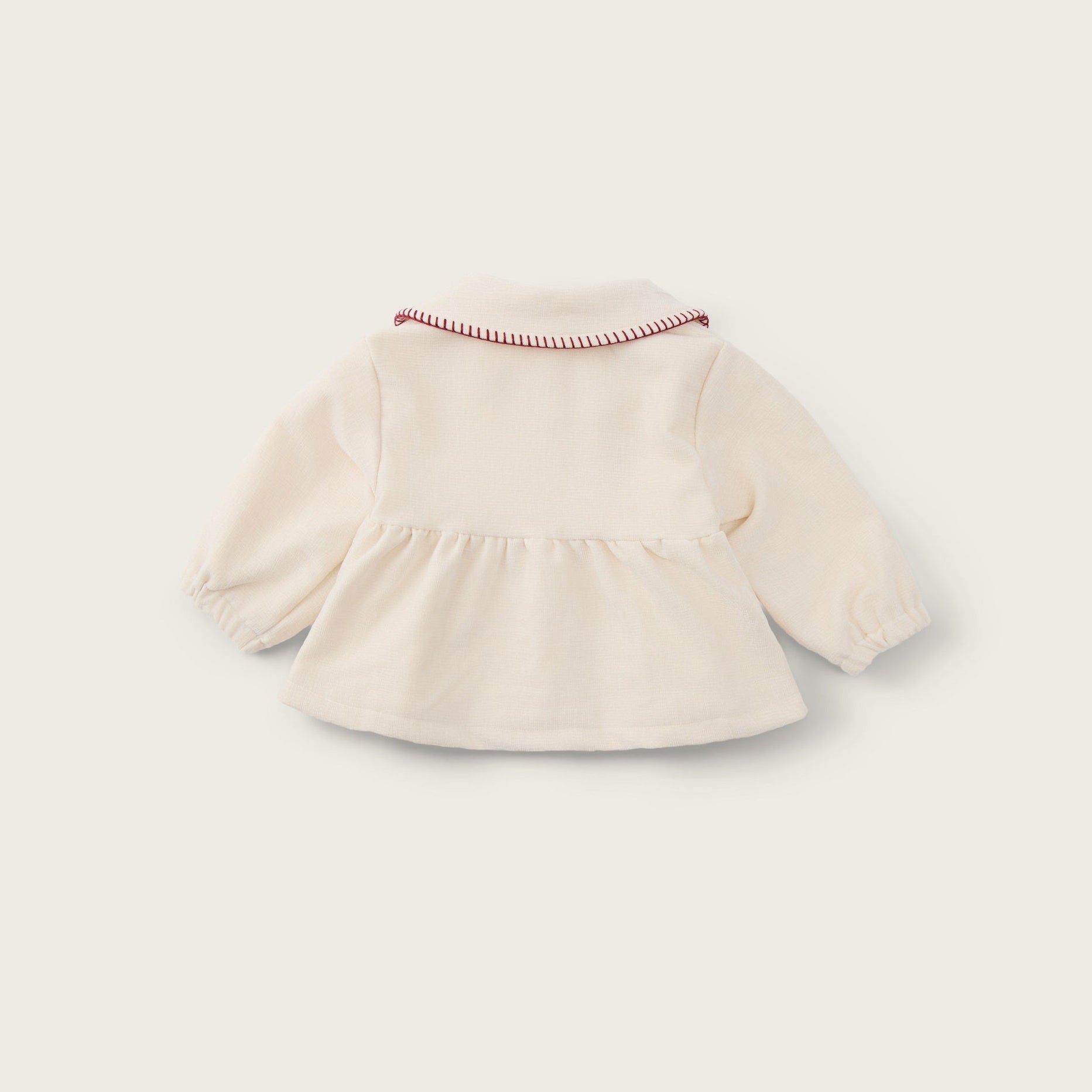 A cream-colored long-sleeve baby top with a ruffled hem and a delicate red-and-white striped collar trim, shown from the back on a light beige background with 'jacinda bebe' and 'lovely kids' text.