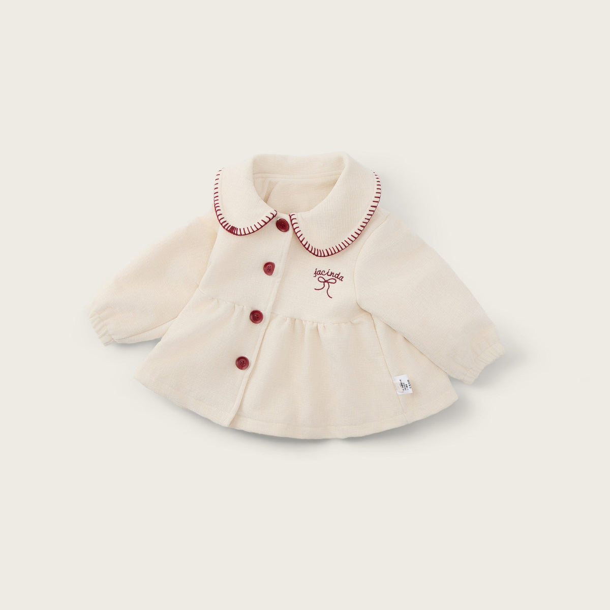 A cream-colored baby cardigan with red buttons and a red embroidered bow on the chest, displayed on a light beige background with 'jacinda bebe' at the top and 'lovely kids' at the bottom.