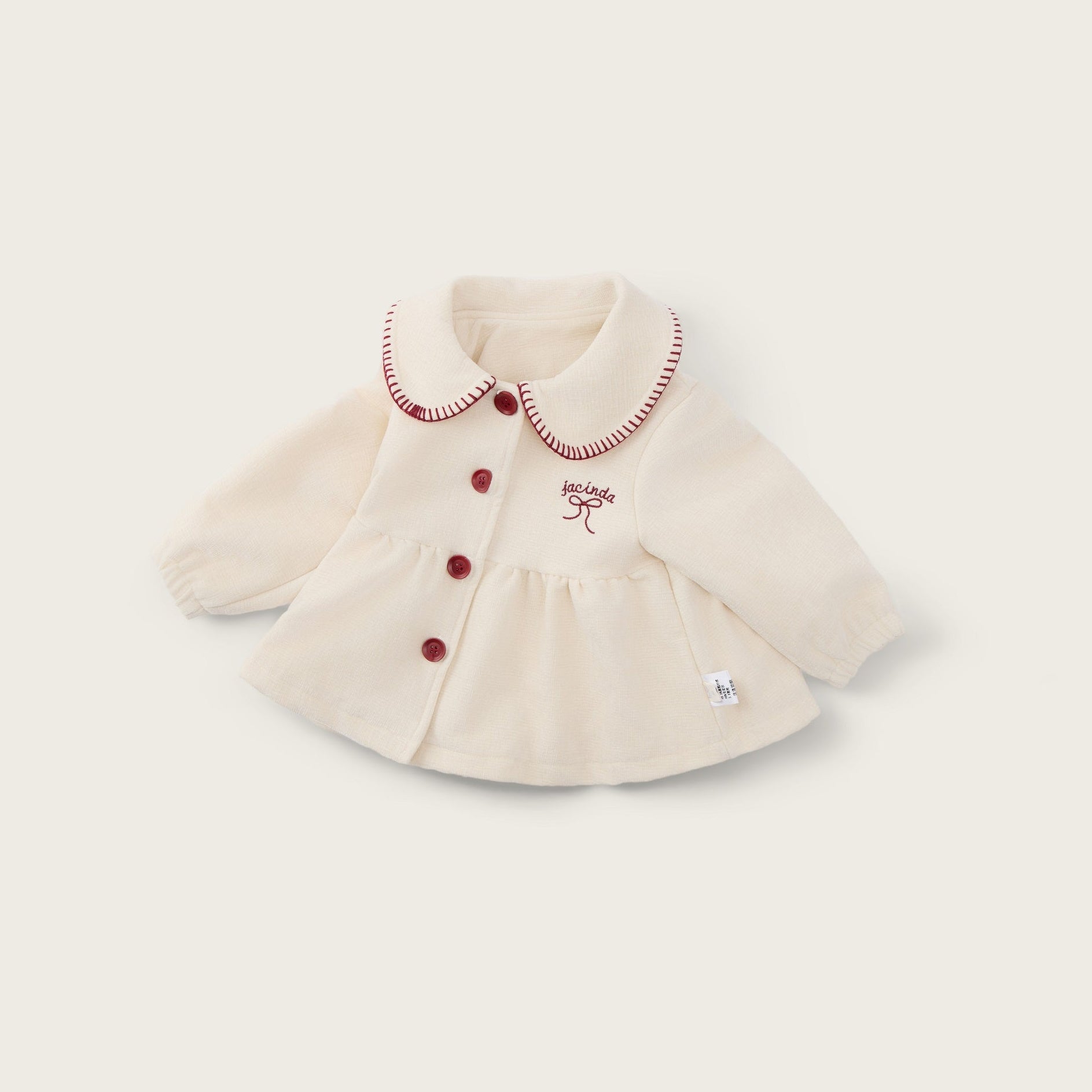 A cream-colored baby cardigan with red buttons and a red embroidered bow on the chest, displayed on a light beige background with 'jacinda bebe' at the top and 'lovely kids' at the bottom.